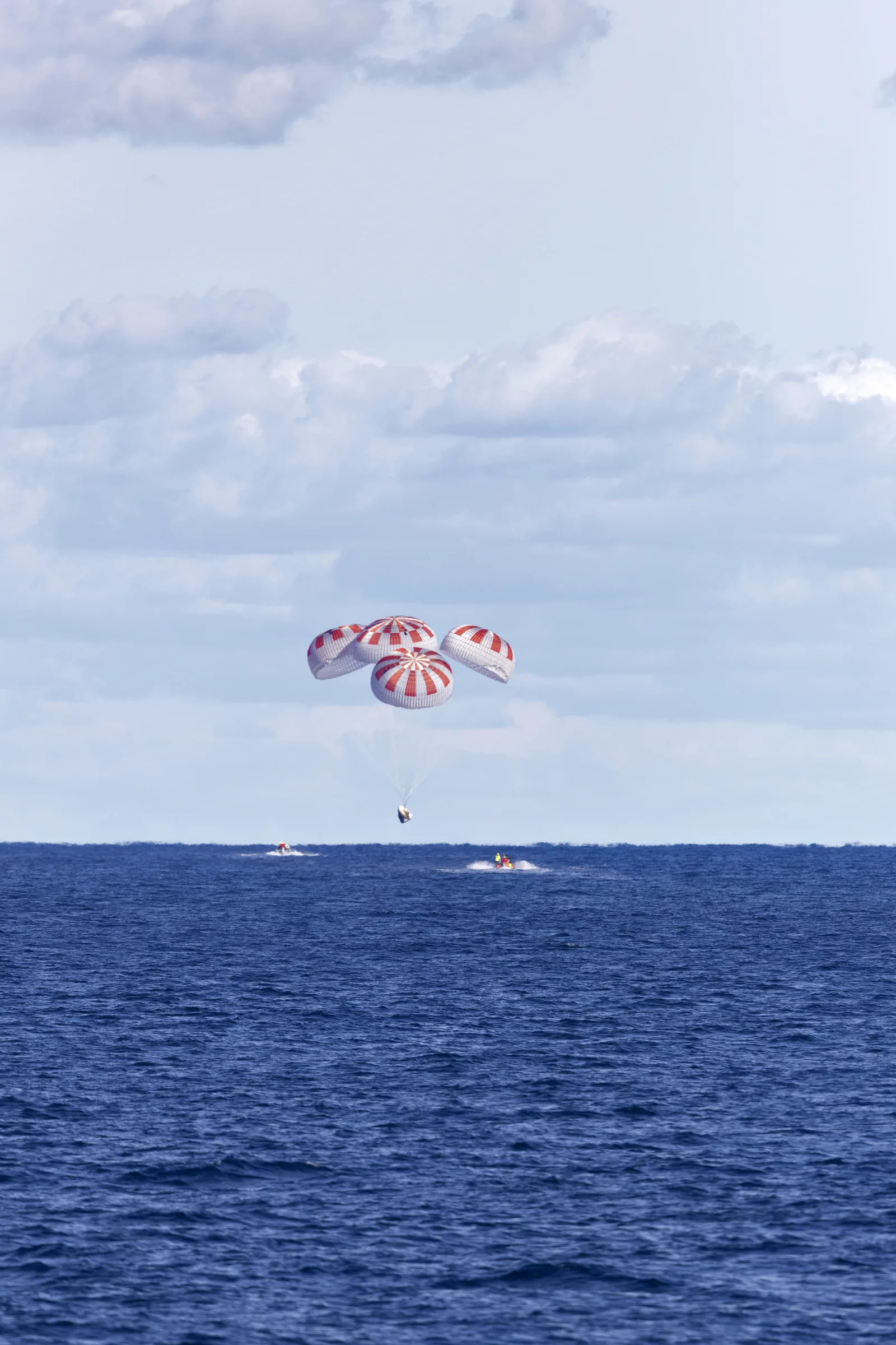 パラシュートを開いて海面へ降下するクルードラゴンのカプセル